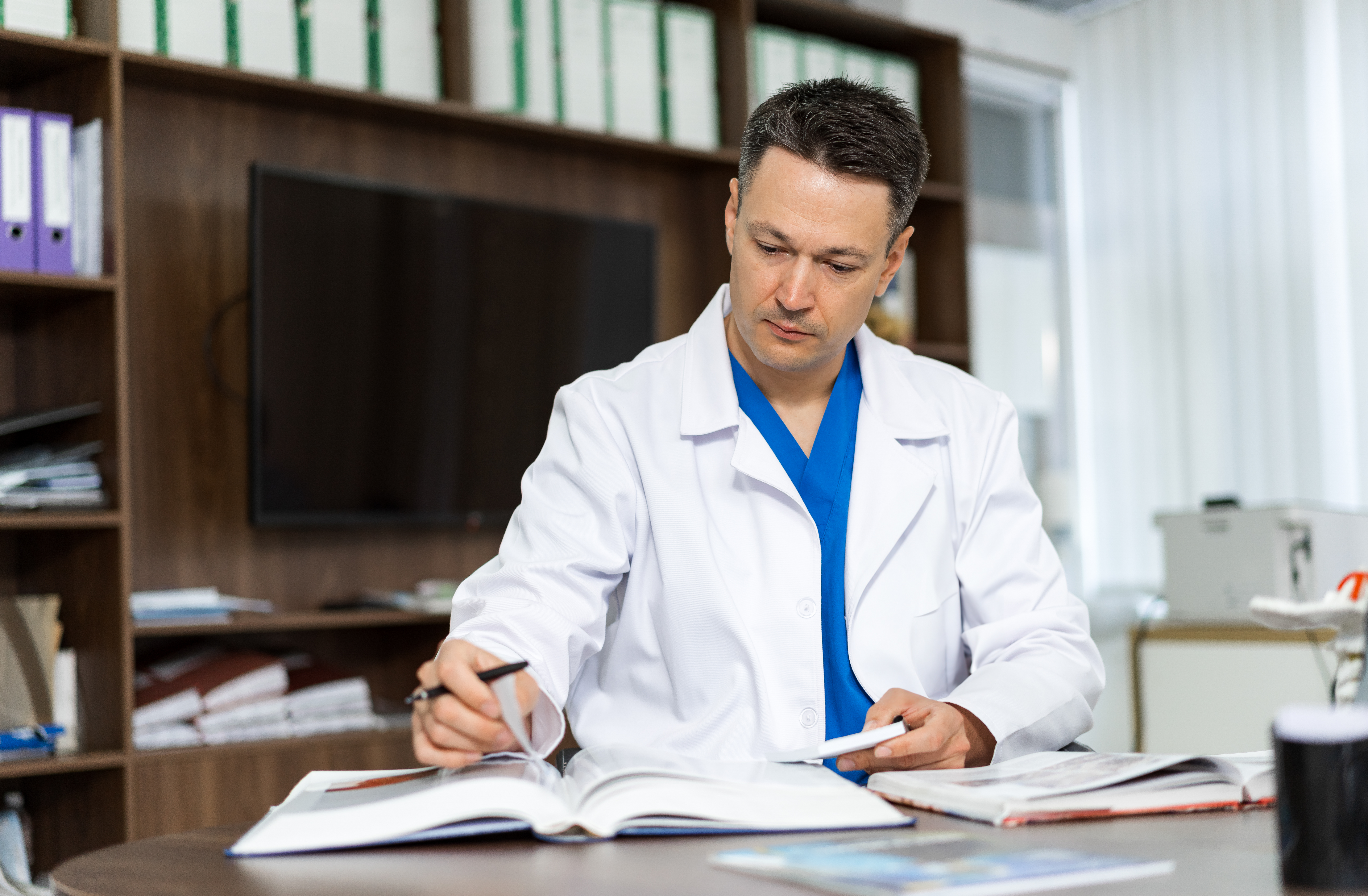 Doctor Reviewing Patient Records In A Modern Office Setting. A Healthcare Professional Is Focused On Reviewing Patient Records At His Desk - Contabilidade em Guarulhos - SP | Boss Contabilidade